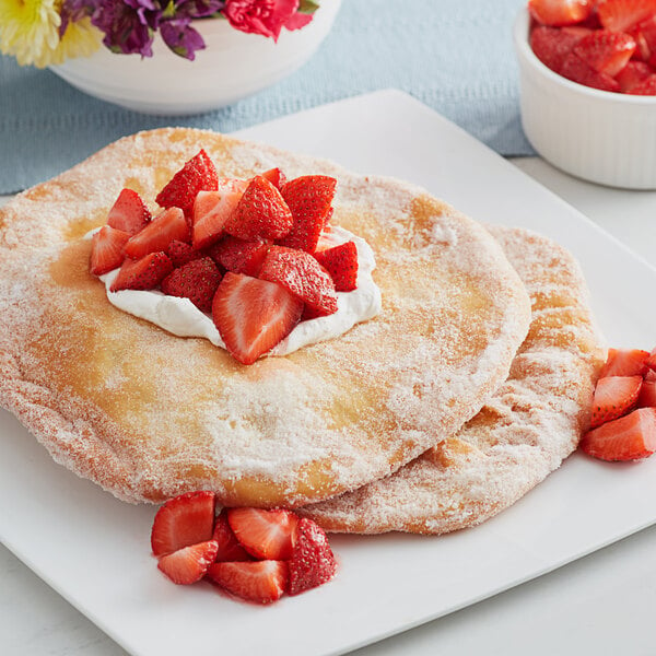 A large fry bread topped with strawberries and whipped cream on a white plate.