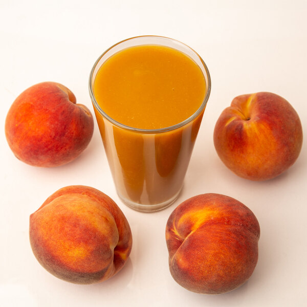 A glass of orange juice with a peach slice on the rim next to a peach.