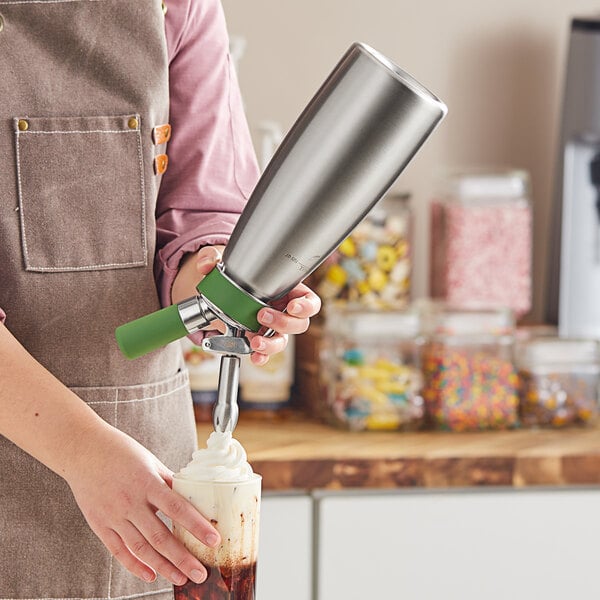 A woman using a stainless steel and green iSi whipped cream dispenser to make a drink.