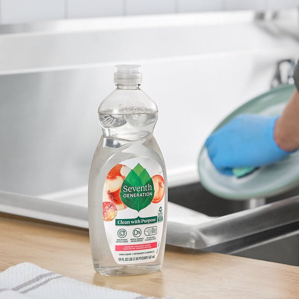 A person cleaning a dish in a kitchen sink with Seventh Generation dishwashing liquid.