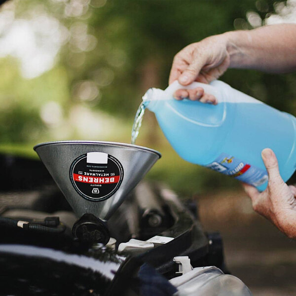 A person pouring blue liquid into a metal funnel.