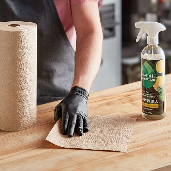 A person wearing black gloves cleaning a roll of Seventh Generation paper towels on a counter.