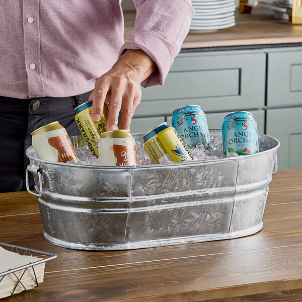 A man holding a yellow Behrens metal tub full of ice and cans.