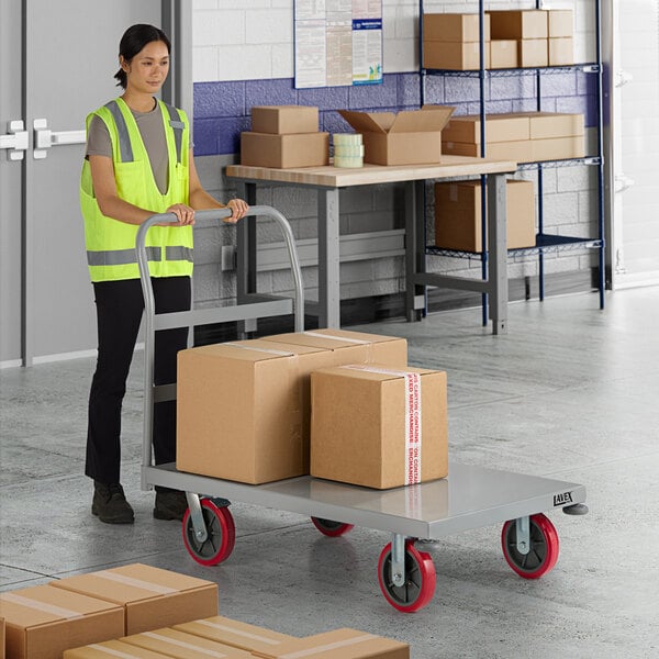 A woman in a yellow safety vest pushing a Lavex Pro heavy-duty steel platform truck with boxes.