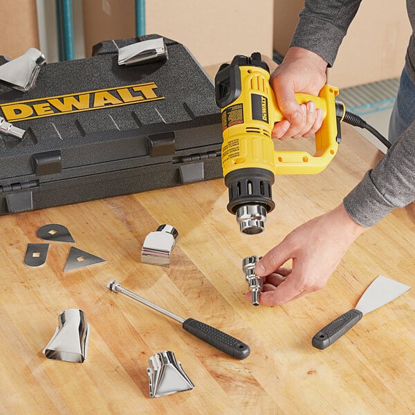 A person using a black DeWalt heat gun kit on a wooden surface.
