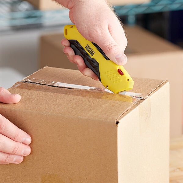 A person using a yellow and black Stanley FATMAX utility knife to cut a box.