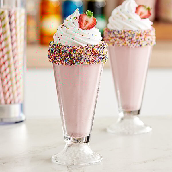 A pink milkshake with sprinkles and a straw on top.