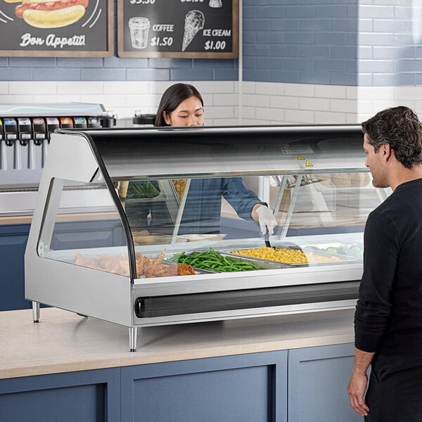 A woman wearing a black shirt putting food in an Alto-Shaam countertop heated display case.