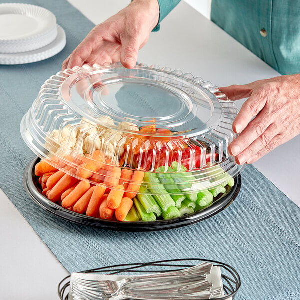 A person holding a Visions black plastic container filled with vegetables.