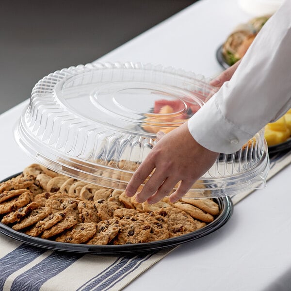 A person holding a Visions black plastic catering tray filled with cookies.