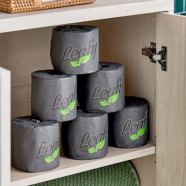 A shelf with a black bag with a green leaf logo containing individually-wrapped Leafy bamboo toilet paper rolls.