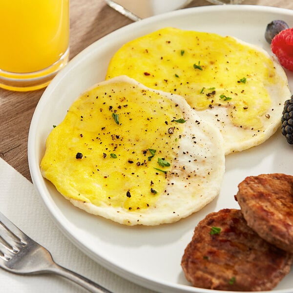 A plate of food with an Abbotsford Farms Cage-Free Egg Patty with cracked black pepper, fruit, and a glass of juice.