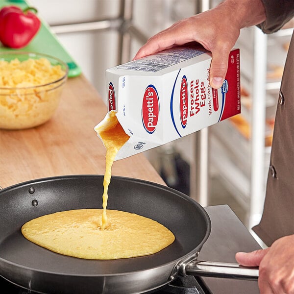 A person pouring yellow liquid into a frying pan of food.