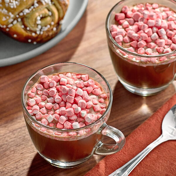 Two cups of hot chocolate with Kraft Mini Peppermint Marshmallows on a table.