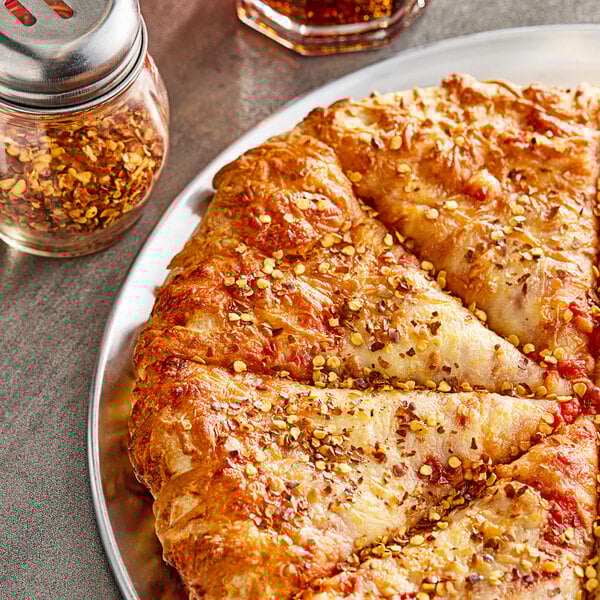 A pizza on a plate with a shaker of Hometown Provisions Crushed Red Pepper Flakes.
