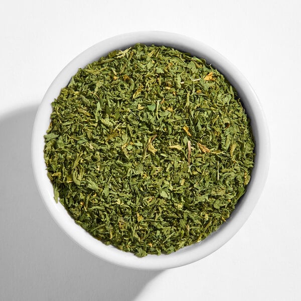 A white bowl filled with dried parsley flakes.