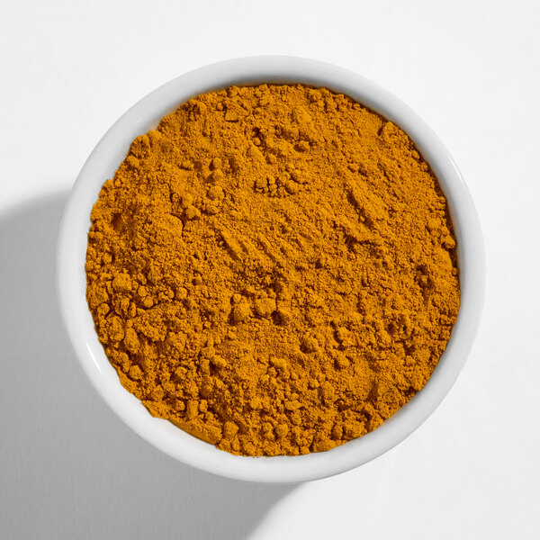 A white bowl filled with ground turmeric powder.