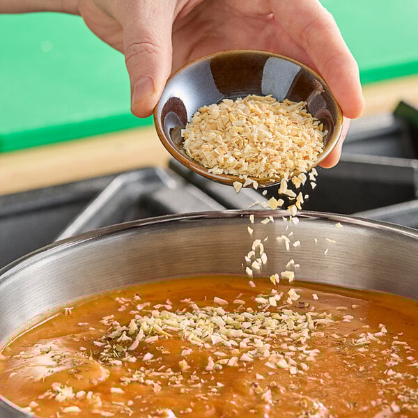 A person holding a bowl of soup garnished with minced onion.