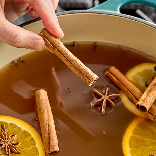 A person holding Hometown Provisions cinnamon sticks over a pot of brown liquid.
