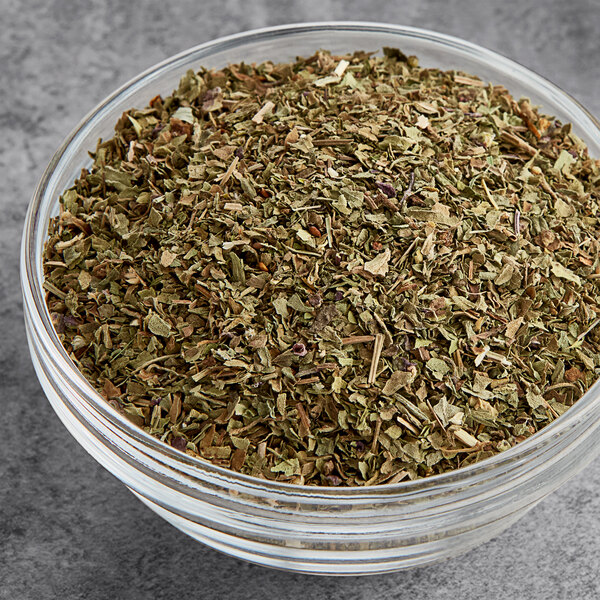 A bowl of Hometown Provisions dried basil leaves on a gray surface.