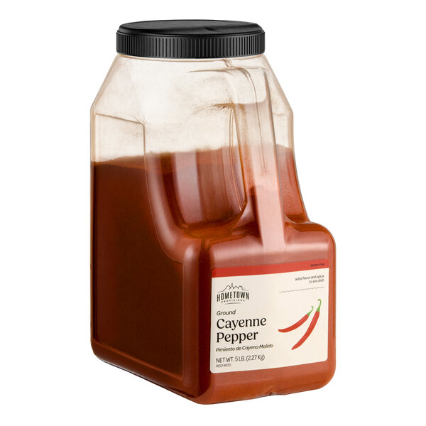 A large plastic container filled with ground cayenne pepper, featuring a black screw-on lid and a label with red chili illustrations.