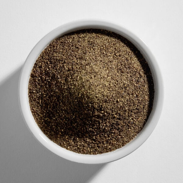 A white bowl filled with coarse ground black pepper viewed from above.