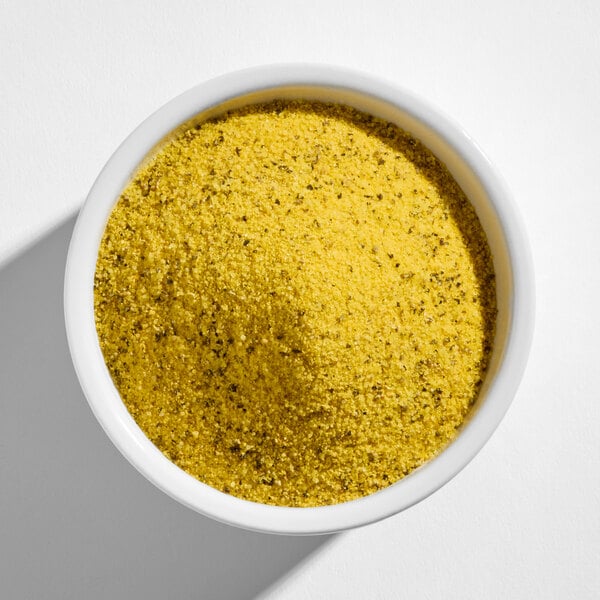 A white bowl filled with a yellow, coarse, and speckled seasoning blend.