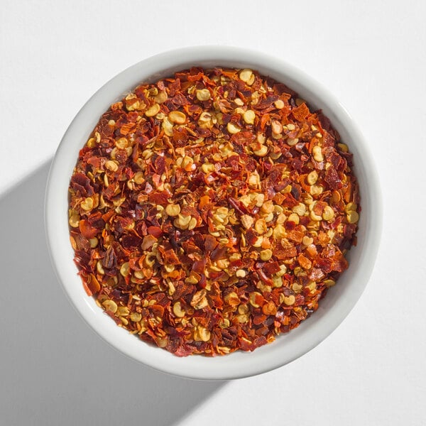 A white bowl filled with crushed red pepper flakes.