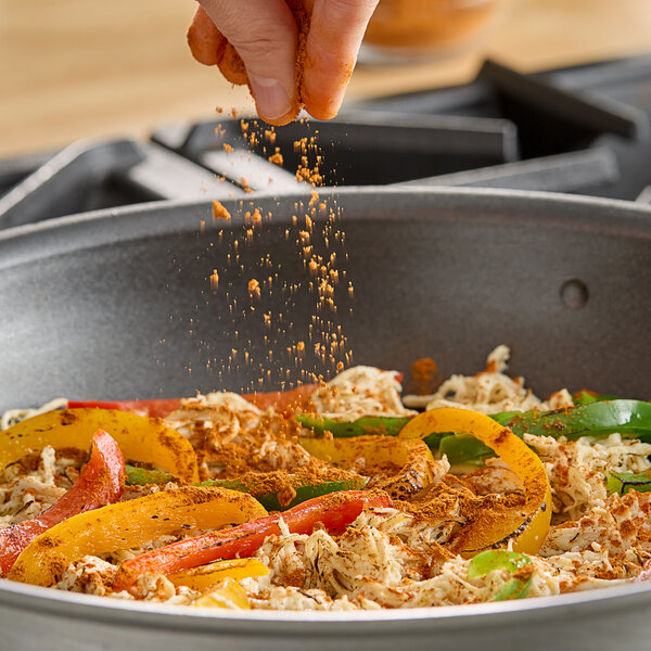 A hand sprinkles Hometown Provisions Cayenne Pepper on food in a pan.