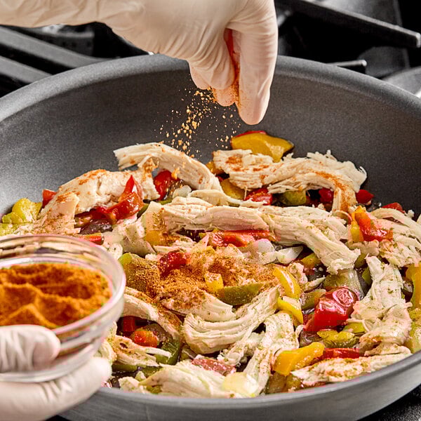 A gloved hand pours Hometown Provisions Taco Seasoning into a glass bowl of food.