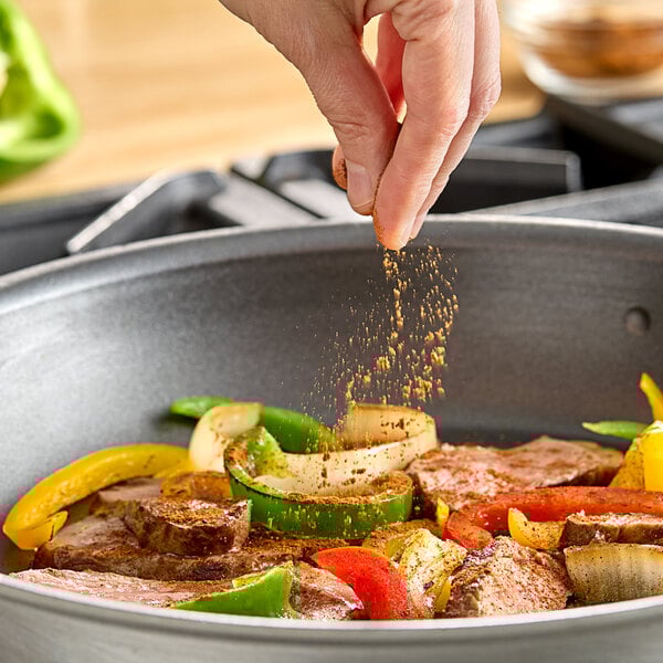 A hand sprinkling Hometown Provisions Chipotle Powder on meat and vegetables in a pan.