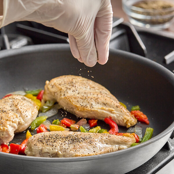 A gloved hand sprinkling Hometown Provisions Table Grind Black Pepper on meat cooking in a pan.