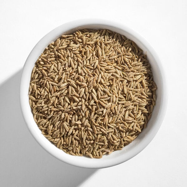 A white bowl filled with whole cumin seeds.
