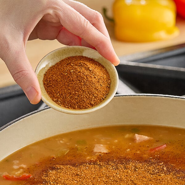 A person pouring Hometown Provisions Cajun Spice into a pot of soup.