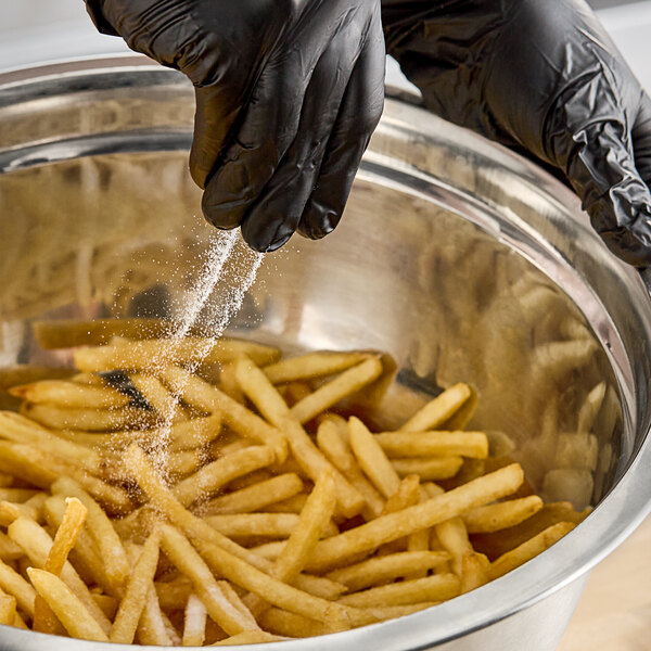 A person in black gloves sprinkling Hometown Provisions fine sea salt on french fries.