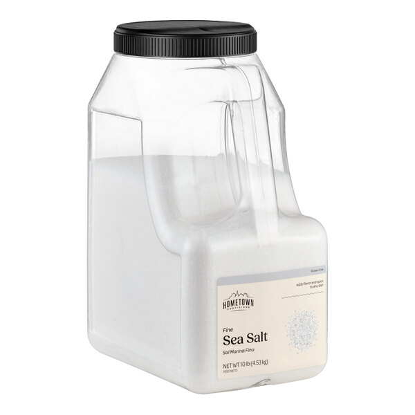 A large clear plastic container with a black screw-on lid, filled with fine white sea salt and labeled on the front.