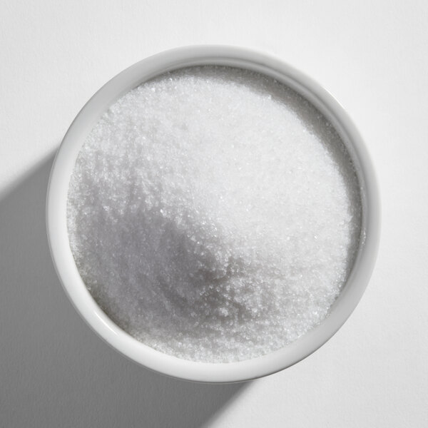 A white bowl filled with fine white granulated substance, likely salt, viewed from above.