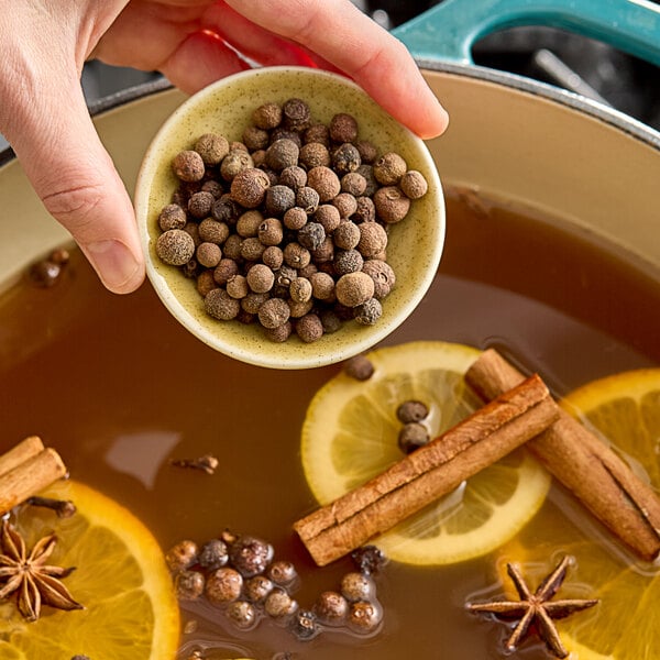 A person pouring Hometown Provisions whole allspice into a bowl of hot liquid.