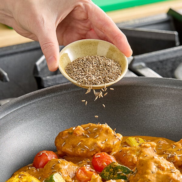 A person pouring Hometown Provisions Cumin Seeds into a pan of food.