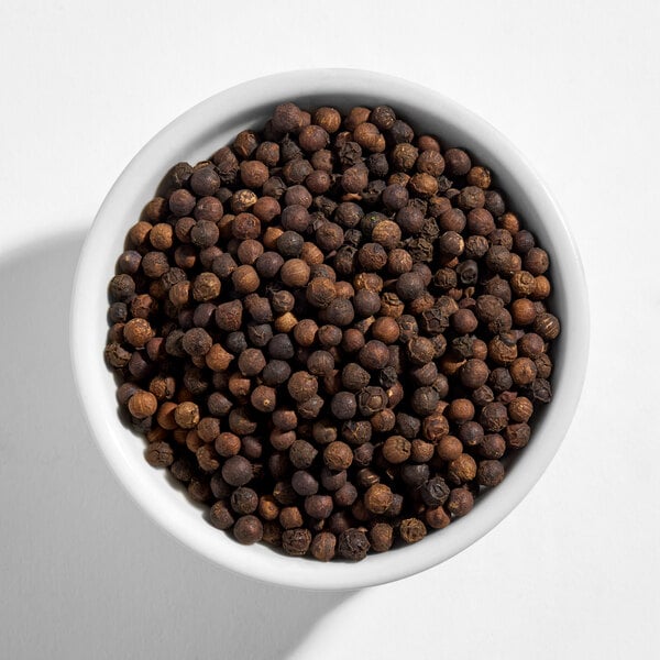A white bowl filled with whole black peppercorns.