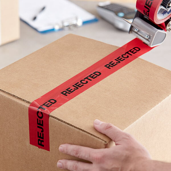 A hand using Tape Logic "Rejected" carton sealer tape to seal a box.