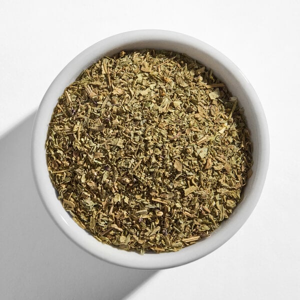 A white bowl filled with dried basil leaves.