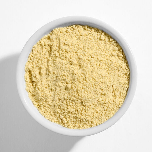 A white bowl filled with ground yellow mustard powder.