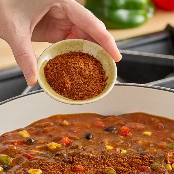 A person pouring Hometown Provisions chili powder into a bowl of food.