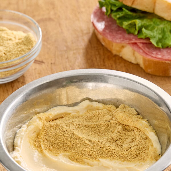 A bowl of food with Hometown Provisions yellow mustard next to a sandwich.