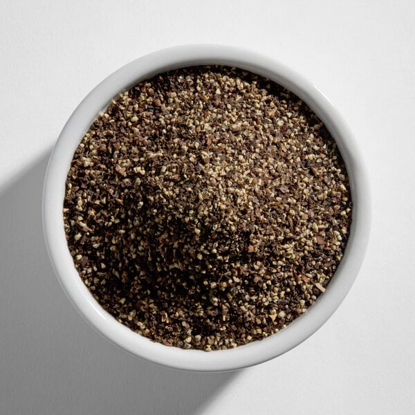 A white bowl filled with coarse ground black pepper.