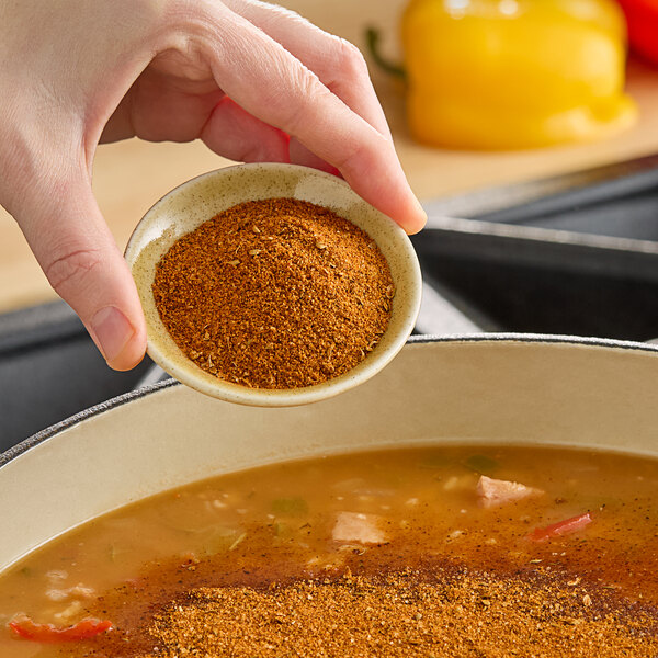 A person pouring Hometown Provisions Cajun Spice into a pot of soup.