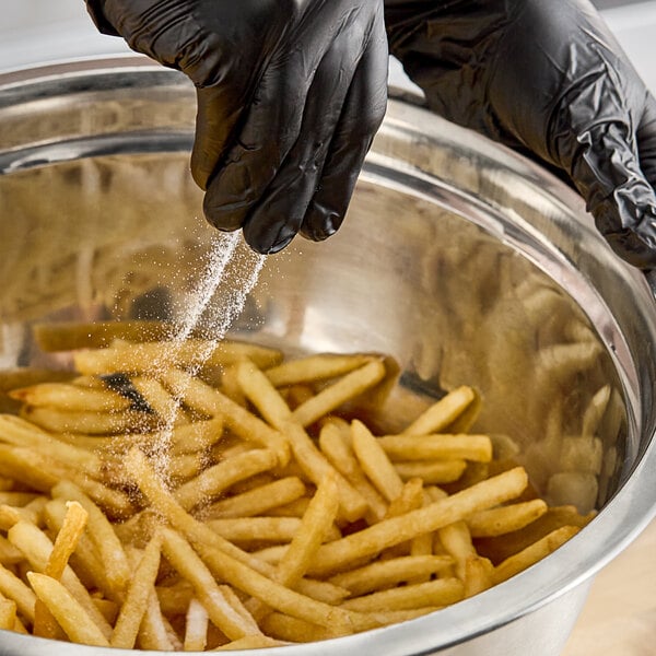 A person wearing black gloves sprinkling Hometown Provisions Fine Sea Salt on french fries.