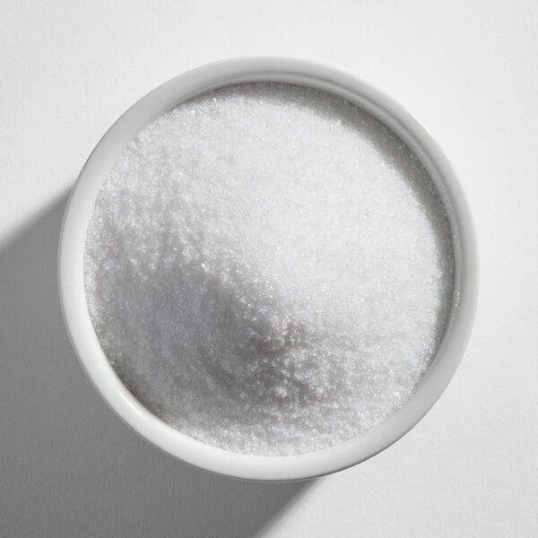 A white bowl filled with fine white granulated substance, likely salt, viewed from above.