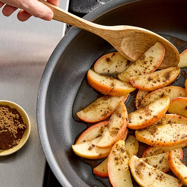 A pan with apples and cloves cooking on a stove next to a bowl of ground cloves.